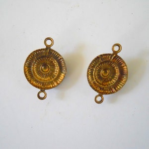 May include: Two gold-toned metal round decorative embellishments with a raised centre circle and concentric circles. Each embellishment has two loops on the top.