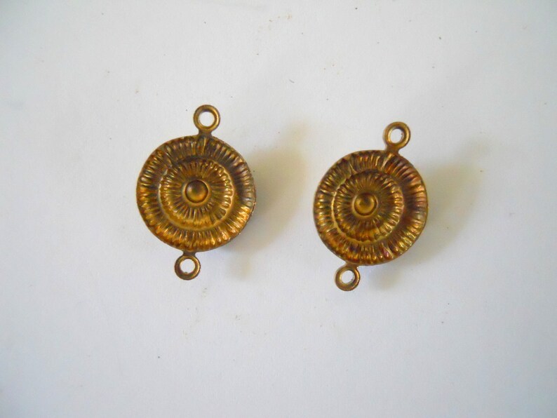 May include: Two gold-toned metal round decorative embellishments with a raised centre circle and concentric circles. Each embellishment has two loops on the top.