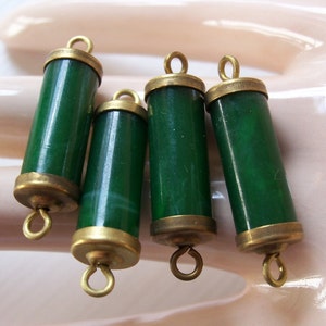 May include: Four green glass beads with brass caps and loops. The beads are cylindrical and have a smooth, polished finish.