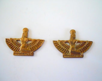 May include: Two gold-colored metal pendants featuring a winged goddess figure with a sun disc on her head. The goddess is depicted in a seated position with her arms outstretched.