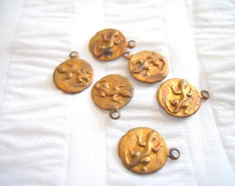May include: Six gold-toned metal charms featuring a raised design of a lizard. Each charm has a small loop for attaching to a necklace or bracelet.