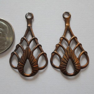 May include: Two copper-colored, openwork teardrop-shaped pendants with a small loop at the top. The design features a central teardrop shape with radiating lines and a woven pattern. A US quarter is next to the pendants.