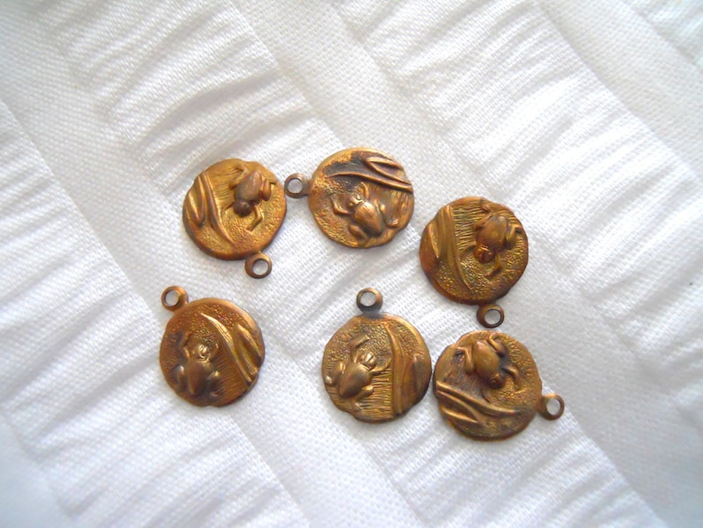 May include: Six gold-toned metal charms with a frog design. Each charm has a loop for attaching to a necklace or bracelet.