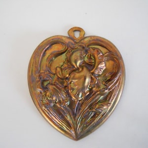 May include: A heart-shaped brass ornament with an embossed design of iris flowers. The ornament has a gold and copper patina and a loop at the top for hanging.