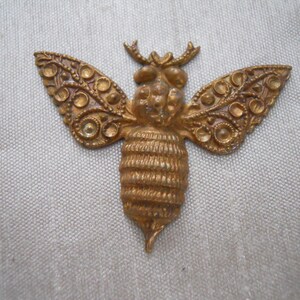 May include: A gold-toned metal bee charm with intricate details. The bee has a detailed body and wings with a raised design.