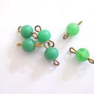 May include: Six green glass beads with gold metal loops. The beads are round and have a smooth surface.