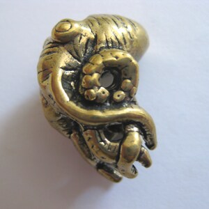 May include: A gold-colored metal octopus figurine with detailed tentacles. The octopus is curled up with its tentacles wrapped around itself.