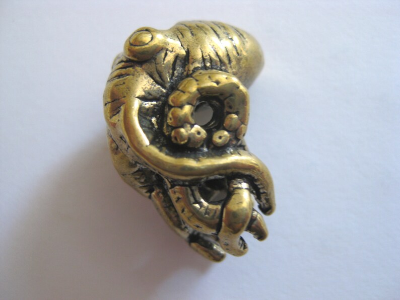 May include: A gold-colored metal octopus figurine with detailed tentacles. The octopus is curled up with its tentacles wrapped around itself.