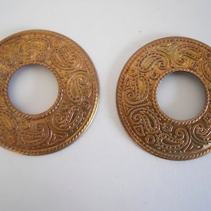 May include: Two gold-colored metal rings with a paisley design. The rings have a large hole in the center.