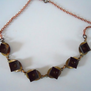 May include: A copper chain necklace with six square-shaped pendants. The pendants are made of brass and have a dark brown finish. The necklace is approximately 18 inches long.
