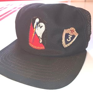 May include: Black baseball cap with a mesh back and a curved brim. The cap features two patches: one with a ghost and lightning bolt design, and another with a shield and the number 3.