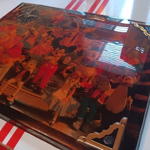 May include: A rectangular wooden box with a glossy finish. The top features a colorful collage of cartoon characters, including Mickey Mouse and other Disney figures. The box has gold-colored metal corner accents and a red and white striped border.