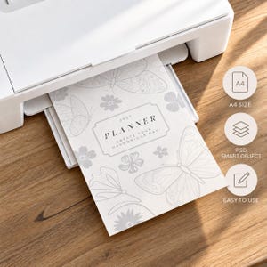 May include: A white printer outputting a sheet of paper featuring a light gray butterfly and floral pattern. The text on the paper reads 2027 PLANNER CREATE YOUR HARMONIOUS DAY. Three circular icons on the right indicate A4 SIZE, PSD SMART OBJECT, and EASY TO USE.