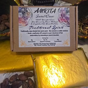 May include: A brown box of "AMRITA Sacred Cacao" with text and a decorative design. The box contains a wrapped bar of cacao. The image also shows cacao beans and other wrapped bars. The text describes the cacao as 100% unroasted and stone ground.