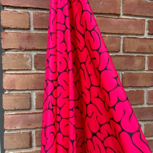May include: Pink fabric with a black brain pattern. The fabric is draped over a brick wall.