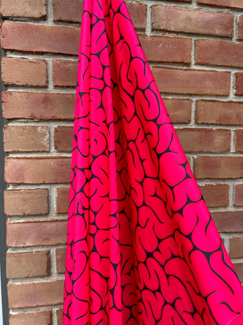 May include: Pink fabric with a black brain pattern. The fabric is draped over a brick wall.