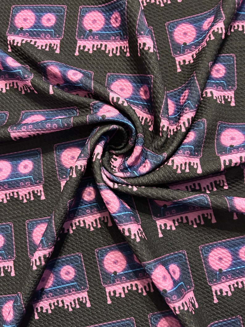 May include: Black fabric with a repeating pattern of pink cassette tapes with neon blue accents. The tapes are dripping pink and have a textured look.