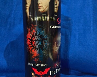 May include: A black stainless steel tumbler with a Supernatural theme. The tumbler features images of the main characters, Dean, Sam, and Castiel, along with the show's logo and the text "Everybody Loves a Good Mystery". The bottom of the tumbler has a red and black image of a car and the text "I Lost My Shoe The Road So Far".