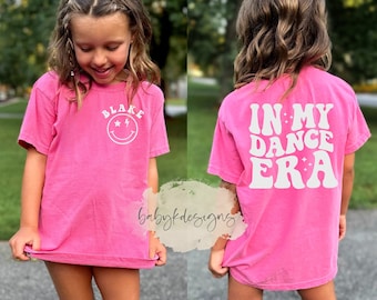 Könnte beinhalten: Rosafarbenes T-Shirt mit einem weißen Smiley und dem Namen "Blake" auf der Vorderseite und dem Text "In My Dance Era" auf der Rückseite.