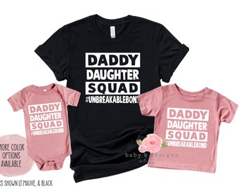 Puede incluir: Un conjunto de tres camisetas en negro y rosa con el texto "Daddy Daughter Squad #UnbreakableBond" impreso en ellas.