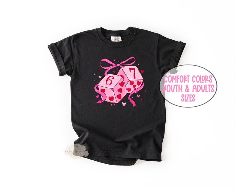 May include: Black t-shirt featuring a graphic of two pink dice with hearts and the numbers 6 and 7. A pink ribbon and the text "Comfort Colors Youth & Adults Sizes" are also visible.