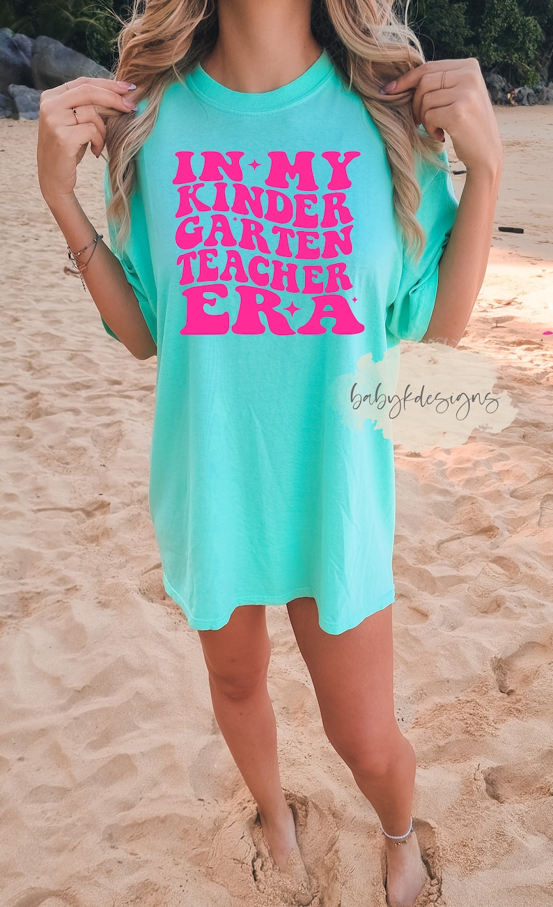May include: A turquoise t-shirt with the text "IN MY KINDERGARTEN TEACHER ERA" in pink retro font.