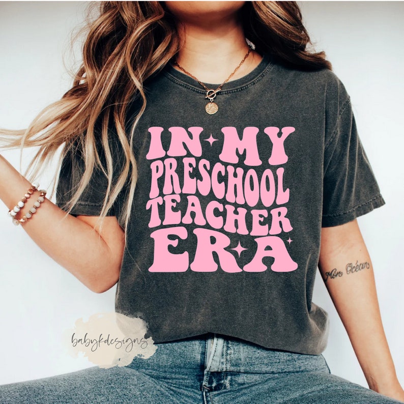 May include: A gray t-shirt with a pink graphic that says "In My Preschool Teacher Era".