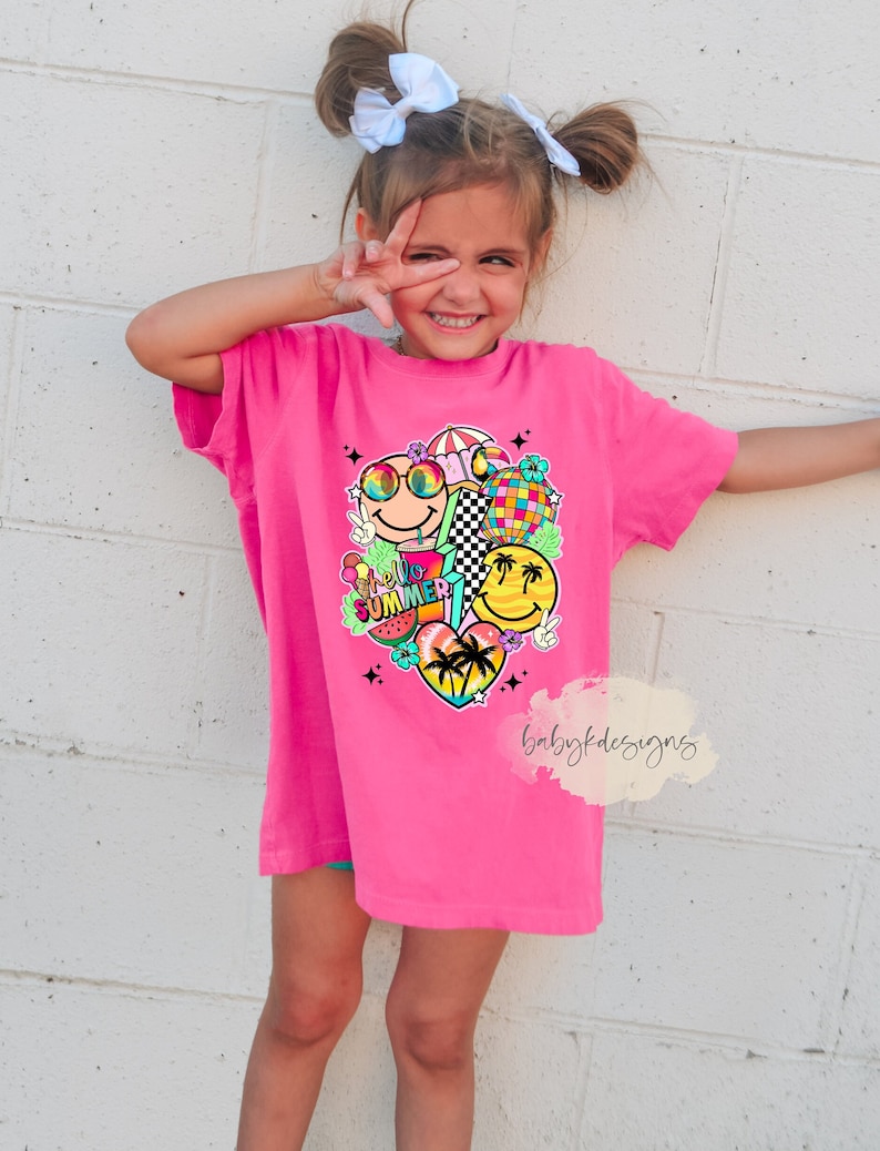 May include: A vibrant pink t-shirt with a colourful graphic design including smiley faces, sunglasses, a watermelon, and the words "Hello Summer". The shirt is worn by a young person.