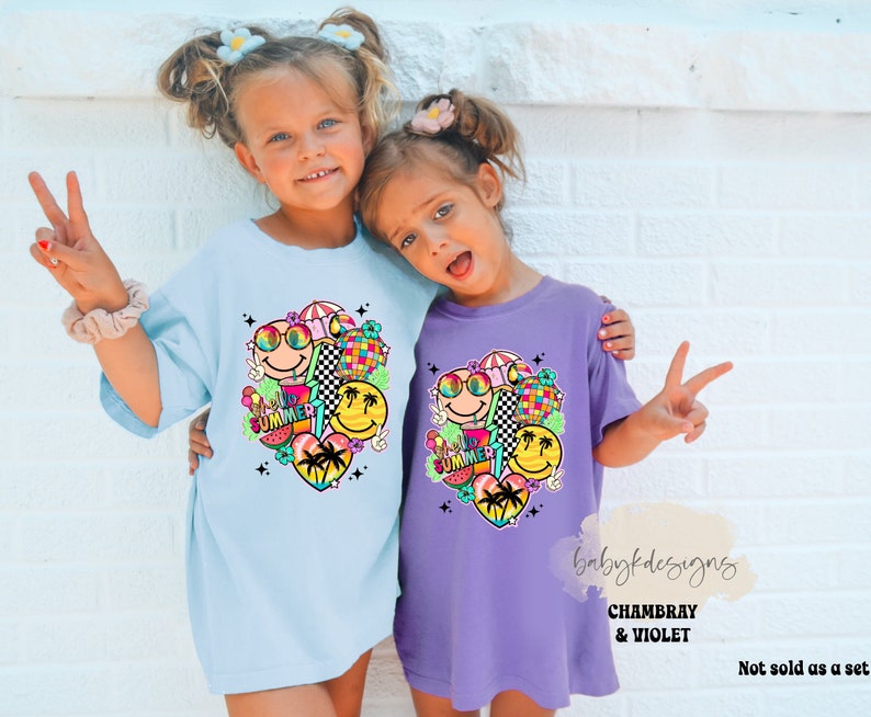 May include: Two children wearing light blue and purple t-shirts. Each shirt features a vibrant graphic with smiley faces, sunglasses, a disco ball, and the word "SUMMER". The t-shirts have a loose, comfortable fit.