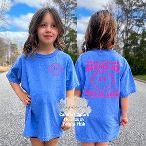 May include: A blue t-shirt with a pink smiley face on the front and the text "Dear person behind me I hope you have a great day Lots of love" on the back.