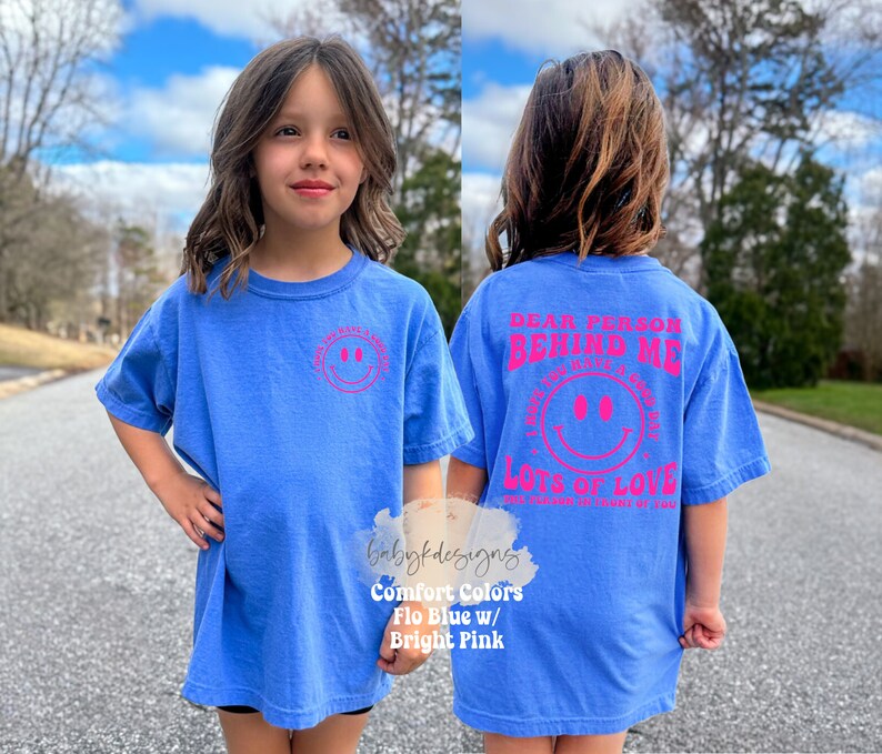 May include: A blue t-shirt with a pink smiley face on the front and the text "Dear person behind me I hope you have a great day Lots of love" on the back.