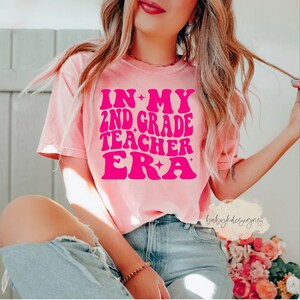 May include: A pink t-shirt with the text "IN MY 2ND GRADE TEACHER ERA" in pink with a star design.