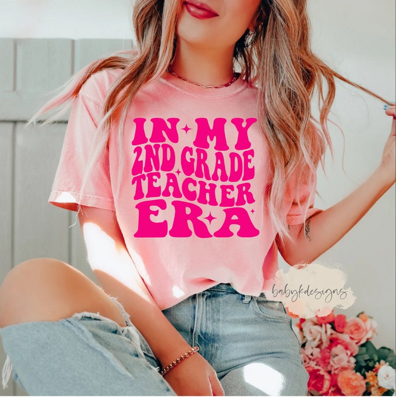May include: A pink t-shirt with the text "IN MY 2ND GRADE TEACHER ERA" in pink with a star design.