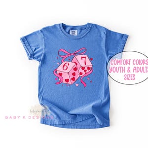 May include: Blue t-shirt featuring a graphic of two dice with the numbers 6 and 7, decorated with pink hearts and a pink ribbon. The text "Comfort Colors Youth & Adults Sizes" is in a white oval.
