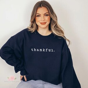 Op de afbeelding: Marineblauwe sweatshirt met het woord "thankful" in het wit in het midden. De tekst is in een eenvoudige lettertype. De sweatshirt heeft lange mouwen en een ronde hals.