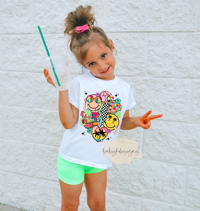 May include: White t-shirt with a colourful "Hello Summer" graphic featuring smiley faces, sunglasses, and a disco ball. The shirt is paired with neon green shorts. A child is holding a drink with a green straw.