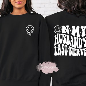 May include: Two black sweatshirts with white text and a smiley face graphic. One sweatshirt says "On My Husband's Last Nerve" and the other has a dripping smiley face.