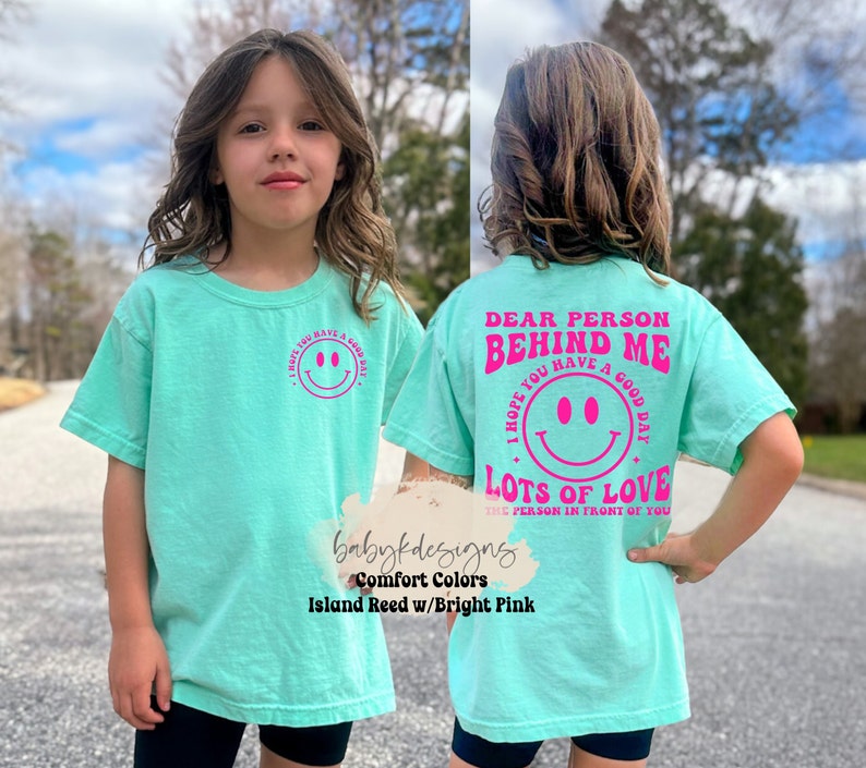 May include: A turquoise blue t-shirt with a pink smiley face and the text "I hope you have a good day" on the front. The back of the shirt has the text "Dear person behind me I hope you have a good day Lots of love the person in front of you" in pink.