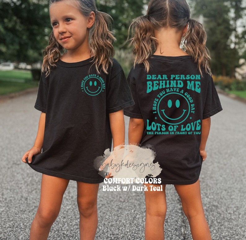 May include: Black t-shirt with a teal smiley face and the text "I hope you have a good day" on the front and "Dear person behind me I hope you have a good day Lots of love the person in front of you" on the back.