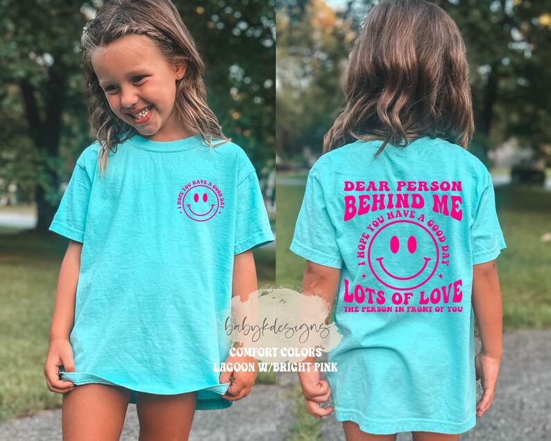 May include: A turquoise blue t-shirt with a pink smiley face on the front and the text "Dear person behind me I hope you have a good day! Lots of love the person in front of you" on the back.