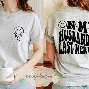 May include: Gray t-shirt with a dripping smiley face on the front and the text "On my husband's last nerve" on the back.