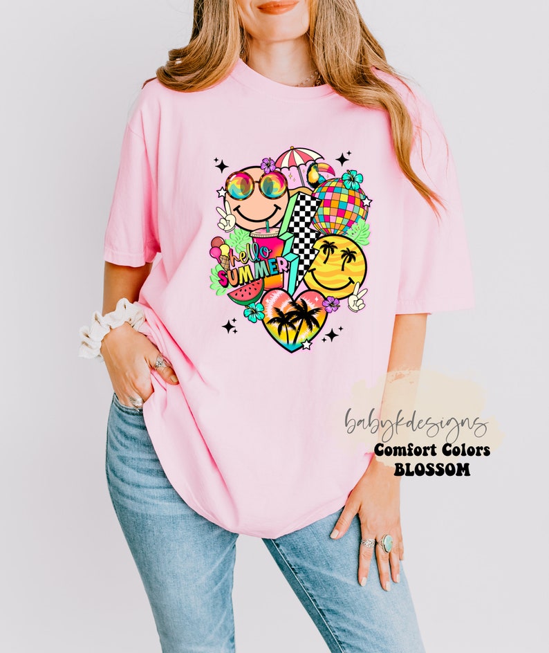 May include: A light pink t-shirt featuring a vibrant graphic. The design incorporates smiley faces, a disco ball, a watermelon slice, and the text "hello summer". The shirt is a comfort colors brand.