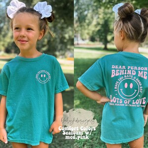 May include: A teal blue t-shirt with a pink graphic that says "Dear Person Behind Me I Hope You Have A Good Day Lots Of Love The Person In Front Of You".