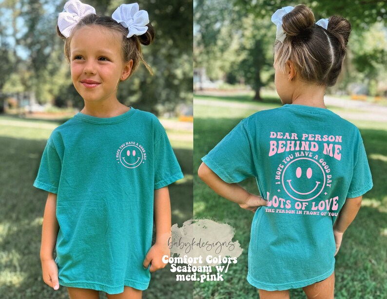 May include: A teal blue t-shirt with a pink graphic that says "Dear Person Behind Me I Hope You Have A Good Day Lots Of Love The Person In Front Of You".