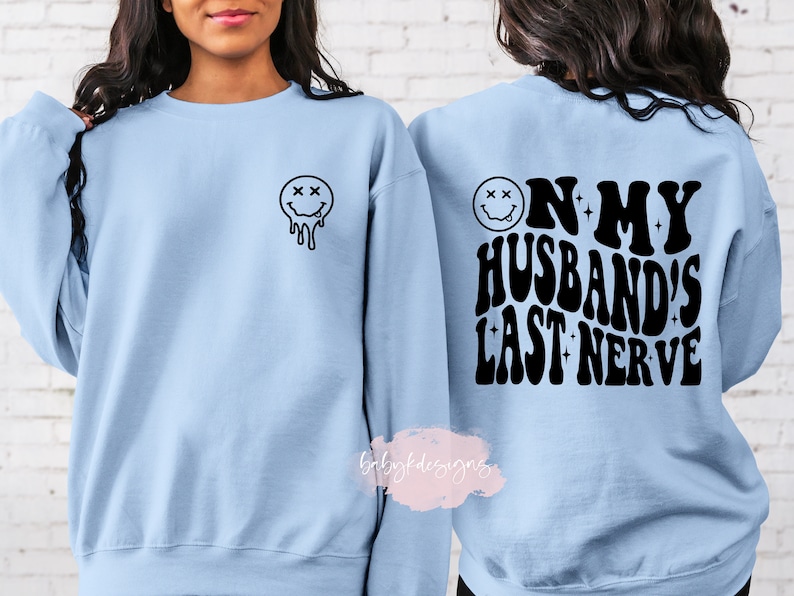 May include: A light blue sweatshirt with a black dripping smiley face on the front and the text "On my husband's last nerve" on the back.