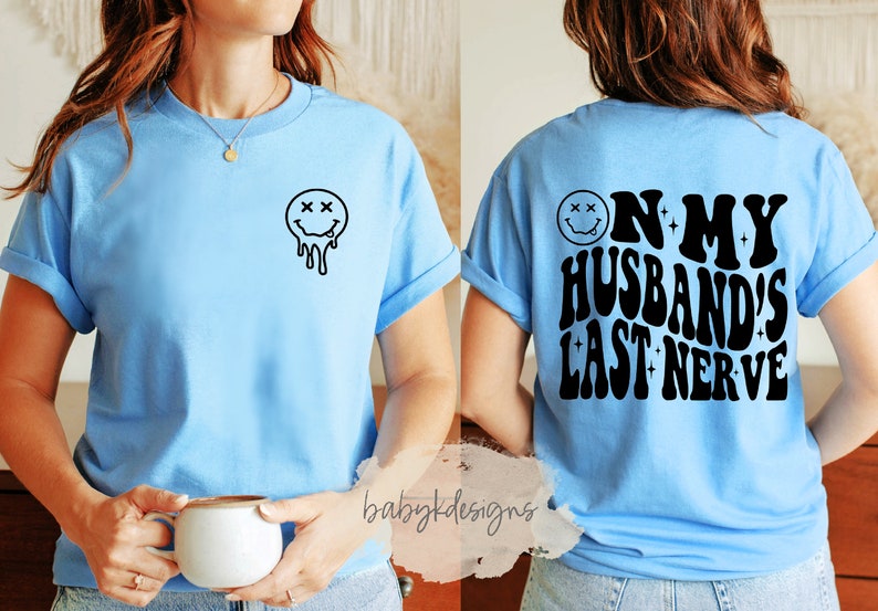 May include: A light blue t-shirt with a black dripping smiley face on the front and the text "On My Husband's Last Nerve" in a retro font on the back.