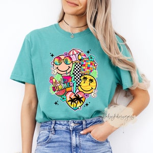 May include: Teal t-shirt with a vibrant graphic of smiley faces, sunglasses, a disco ball, and the words "Hello Summer." The design incorporates a watermelon slice, ice cream, and palm trees. The shirt is made of a soft material.