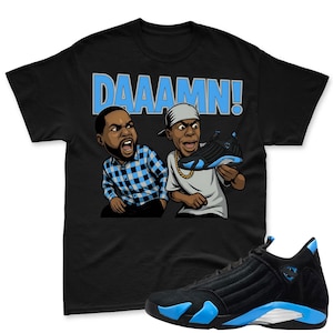May include: Black t-shirt with the word "DAAAMN!" in light blue, featuring cartoon illustrations of two men. A pair of black and light blue sneakers are in the foreground, with a matching sneaker held by one of the cartoon characters.