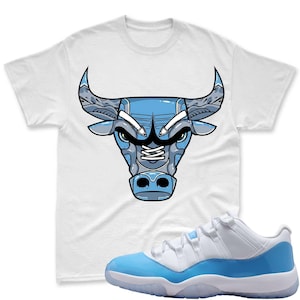 May include: A white t-shirt with a blue bull head design and a pair of white and light blue trainers with a translucent sole. The design is a nod to the Chicago Bulls basketball team.