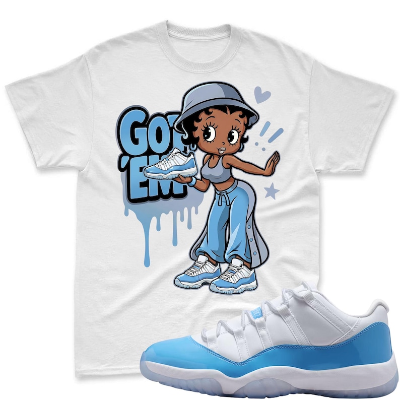 Op de afbeelding: Wit T-shirt met een cartoonafbeelding van een vrouw die een blauw-witte sneaker vasthoudt, met de tekst "Got 'Em" in het blauw. Een paar blauw-witte sneakers op de voorgrond.